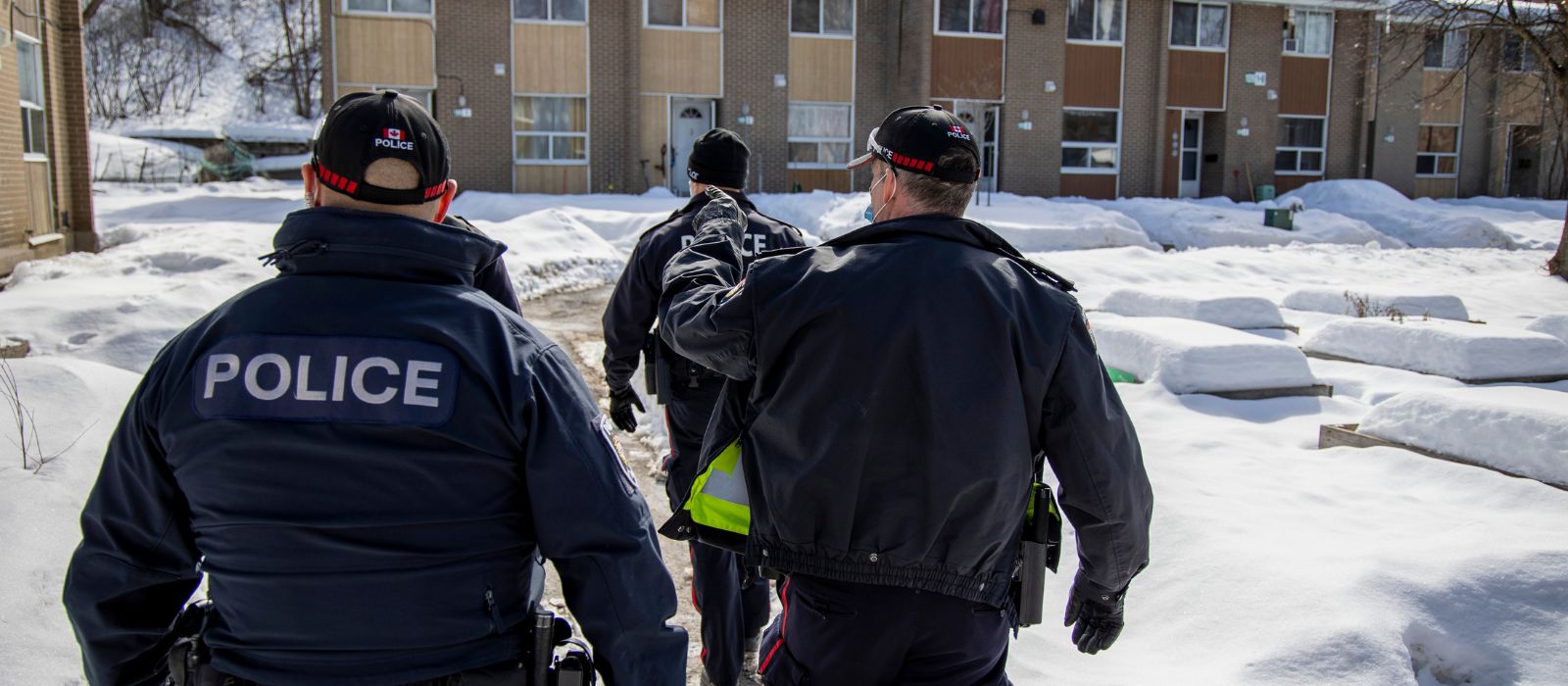 Un groupe de membres du Service de police d'Ottawa marchant dans un complexe résidentiel en hiver.