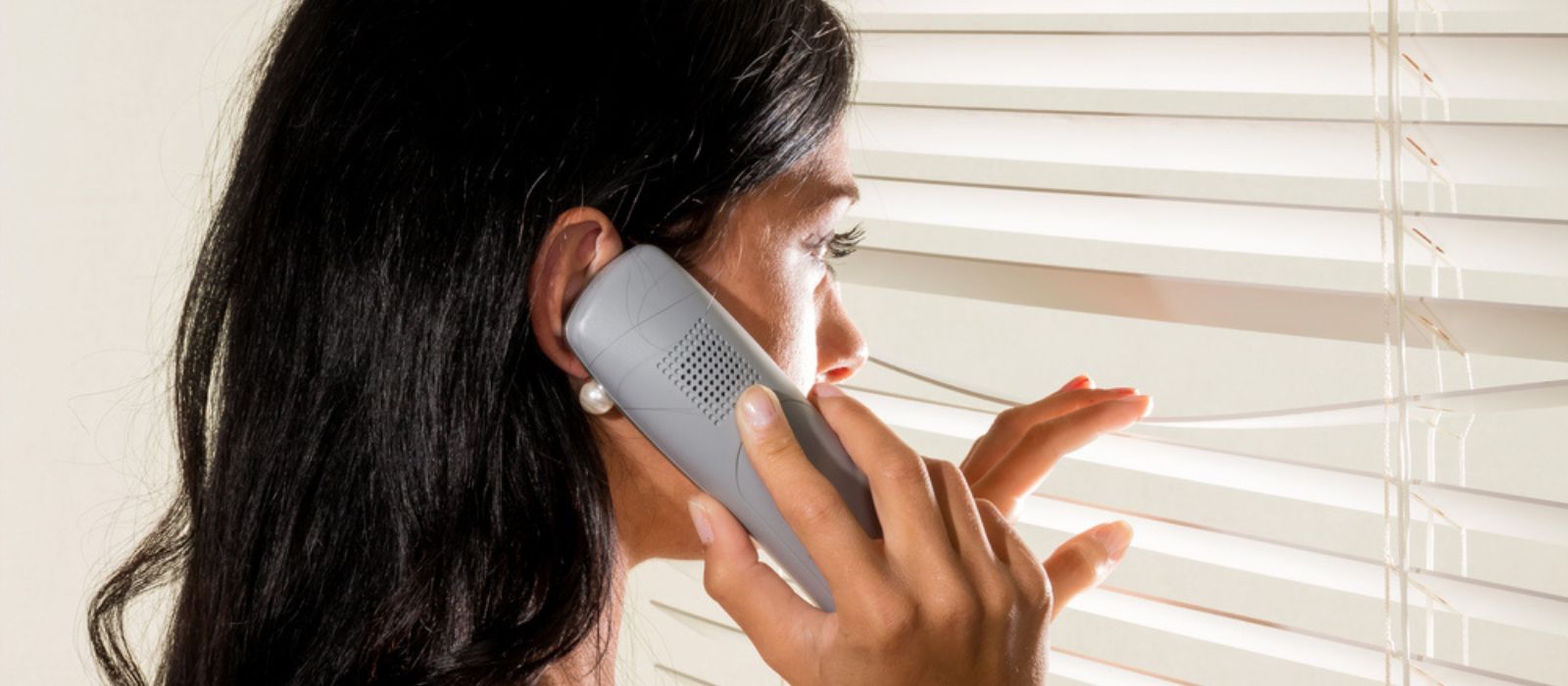 Une voisine inquiète regarde par sa fenêtre tout en téléphonant.