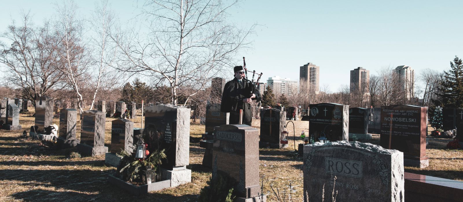 A member of the Ottawa Police Pipe Band playing the bagpipes in a cemetery.